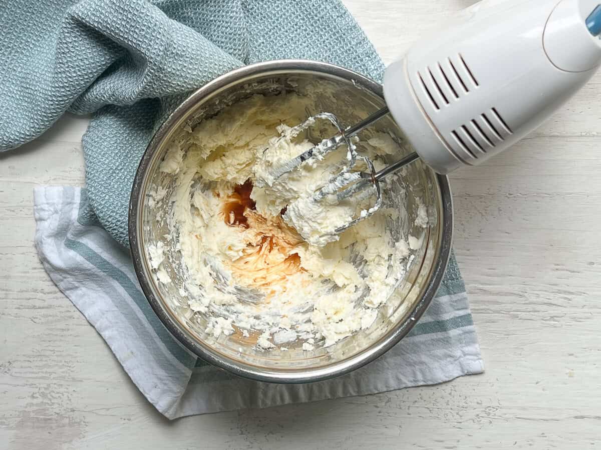 A handmixer blending vanilla into cream cheese frosting.