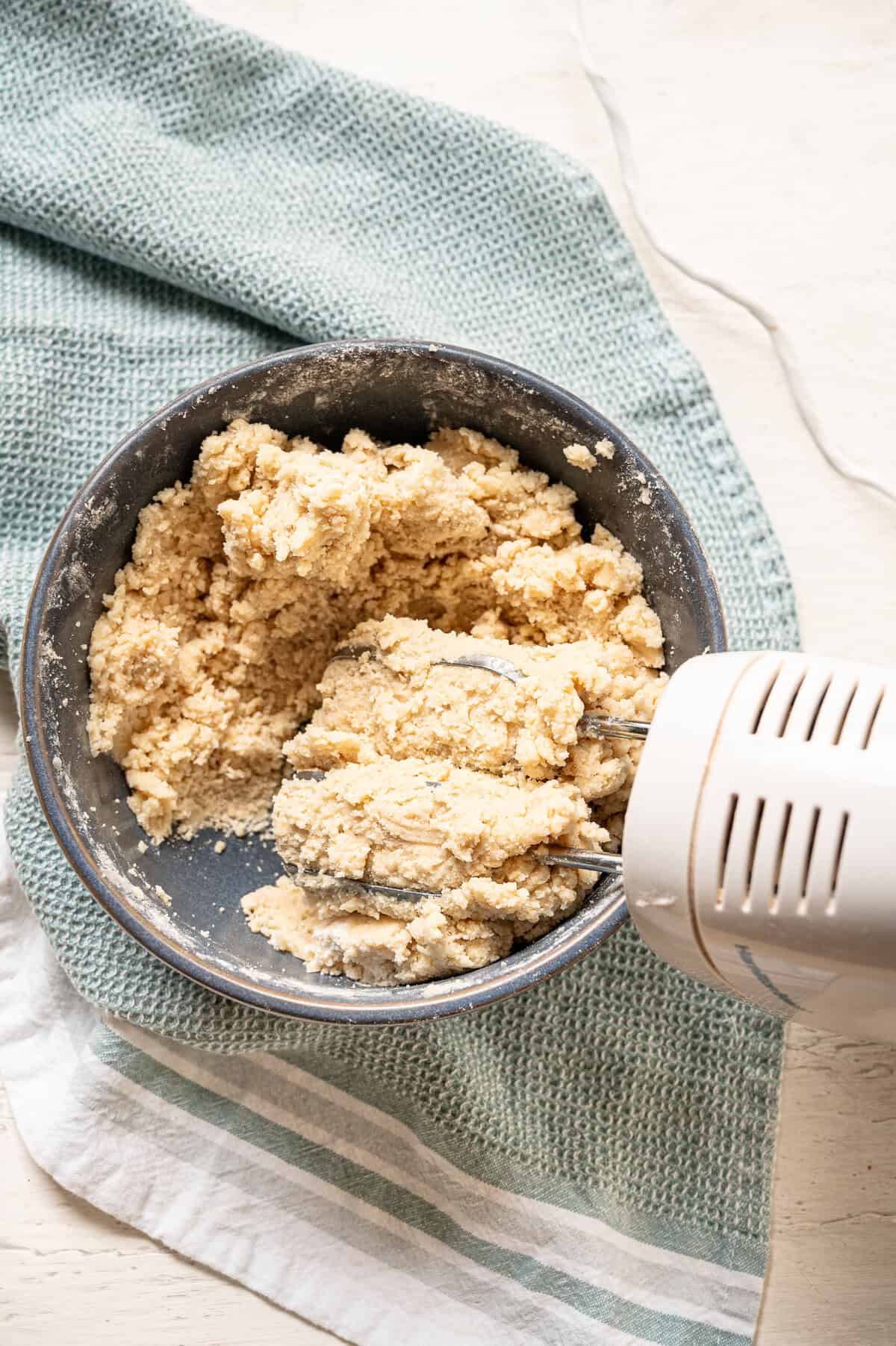 Wet and dry ingredients for cookies being mixed with a hand mixer.