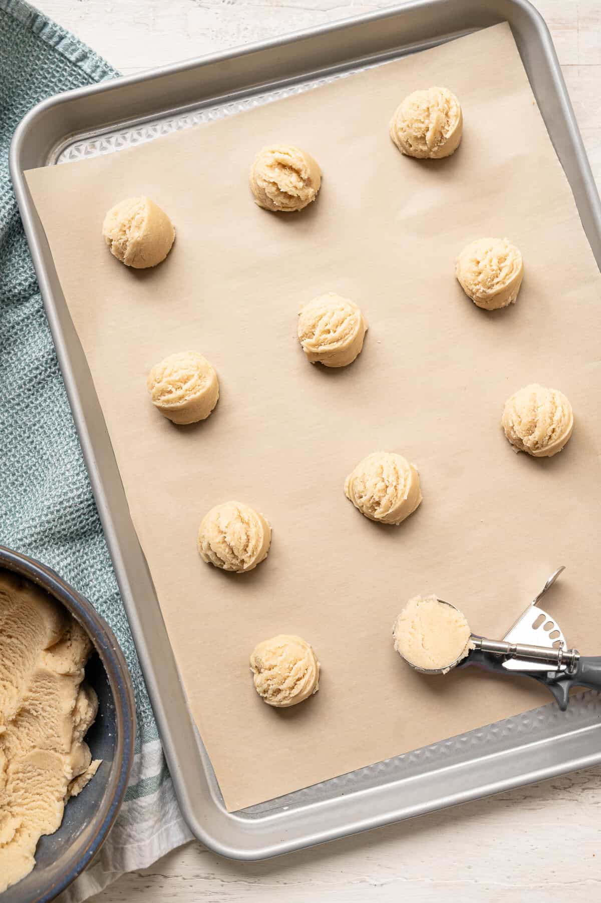 A cookie scoop being used to put dough balls on a parchment-lined baking sheet.