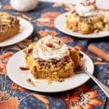 Pumpkin dump cake on a plate with homemade whipped cream and chopped pecans on top.