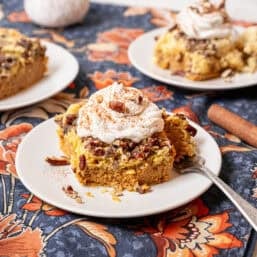 Pumpkin dump cake on a plate with homemade whipped cream and chopped pecans on top.