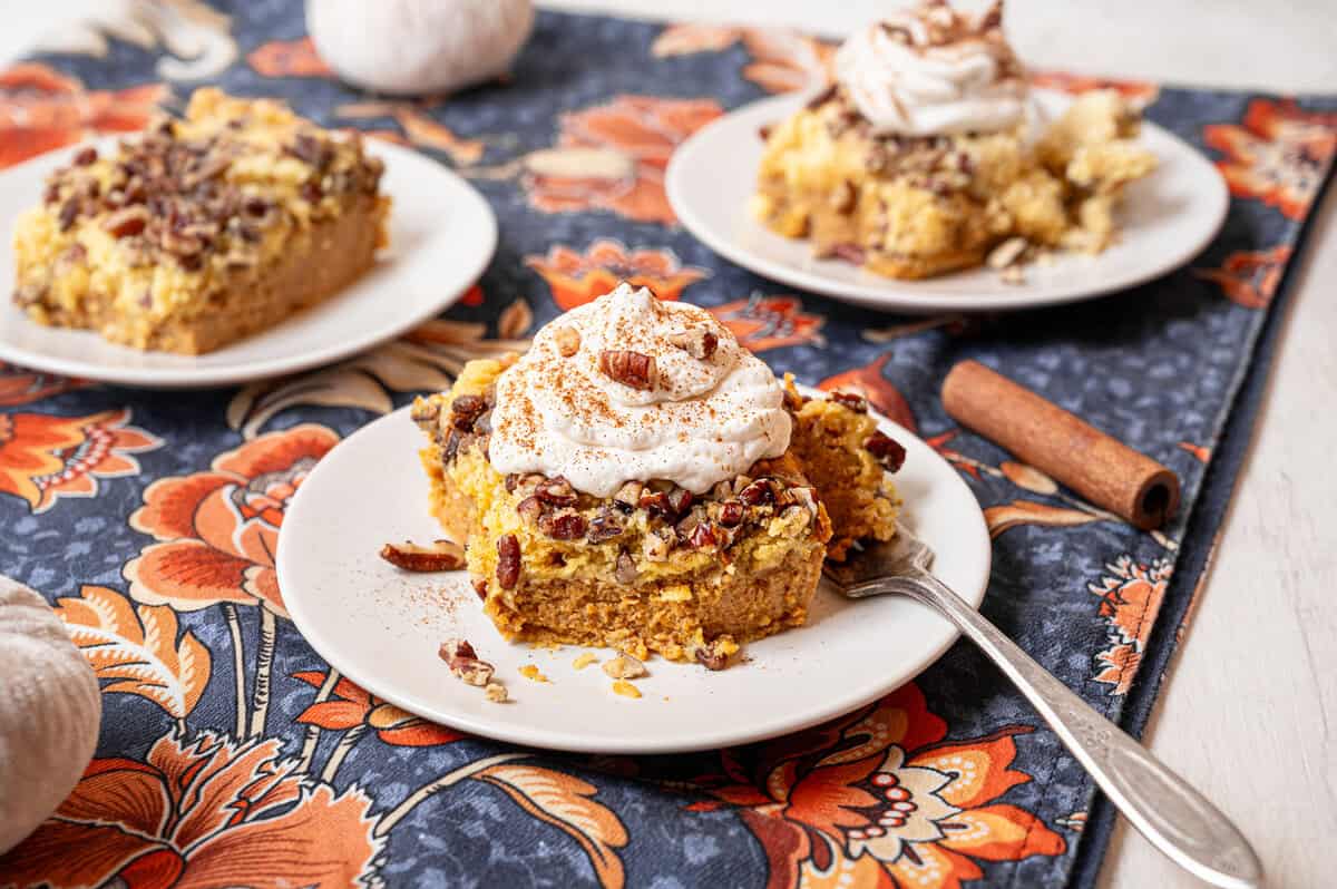 Pumpkin dump cake on a plate with homemade whipped cream and chopped pecans on top.