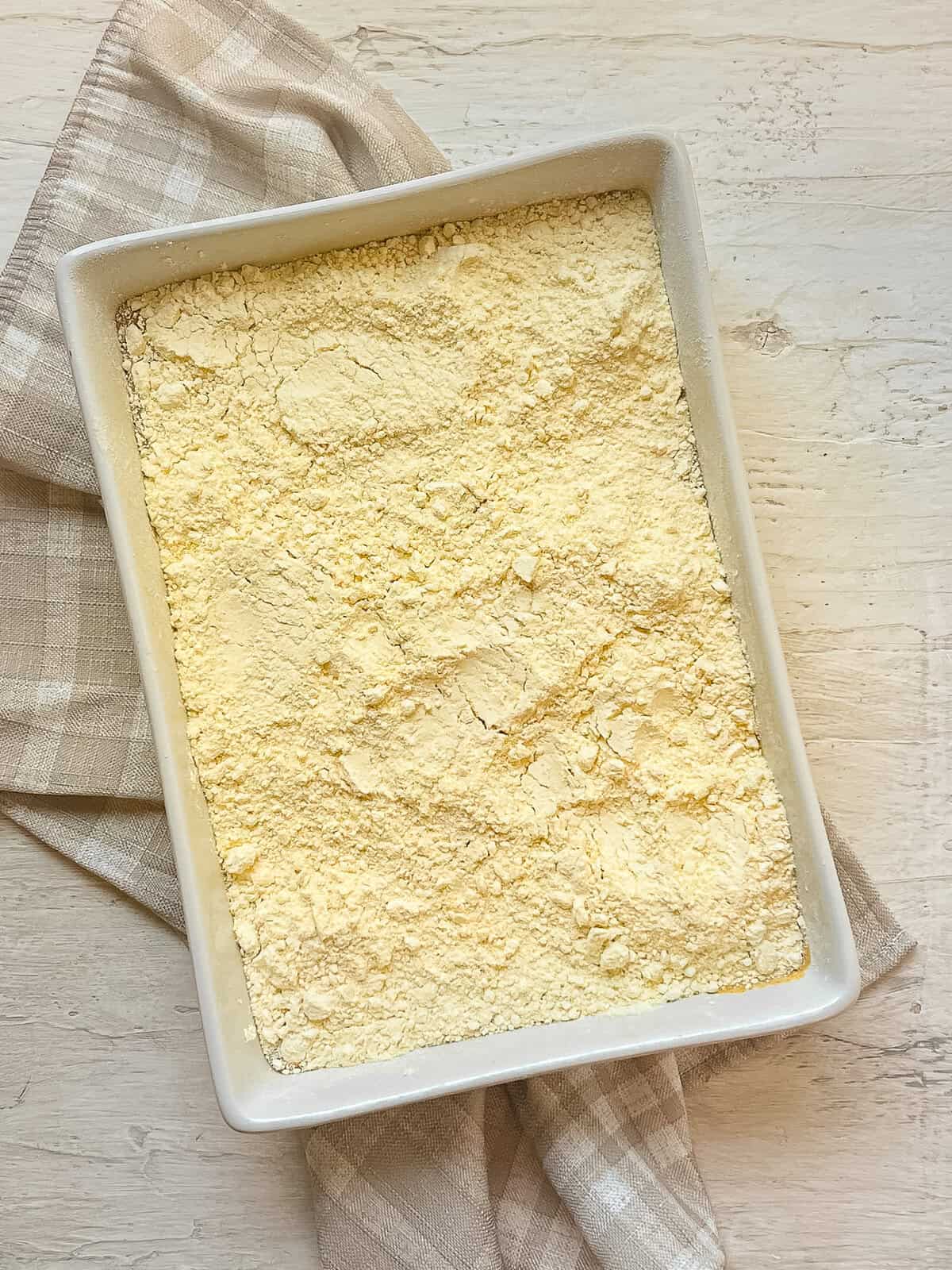 Yellow cake mix sprinkled over wet ingredients for pumpkin dump cake.
