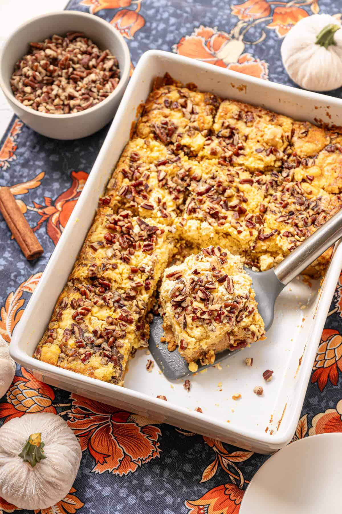Pumpkin dump cake served from a white casserole dish with a small bowl of chopped pecans on the side.