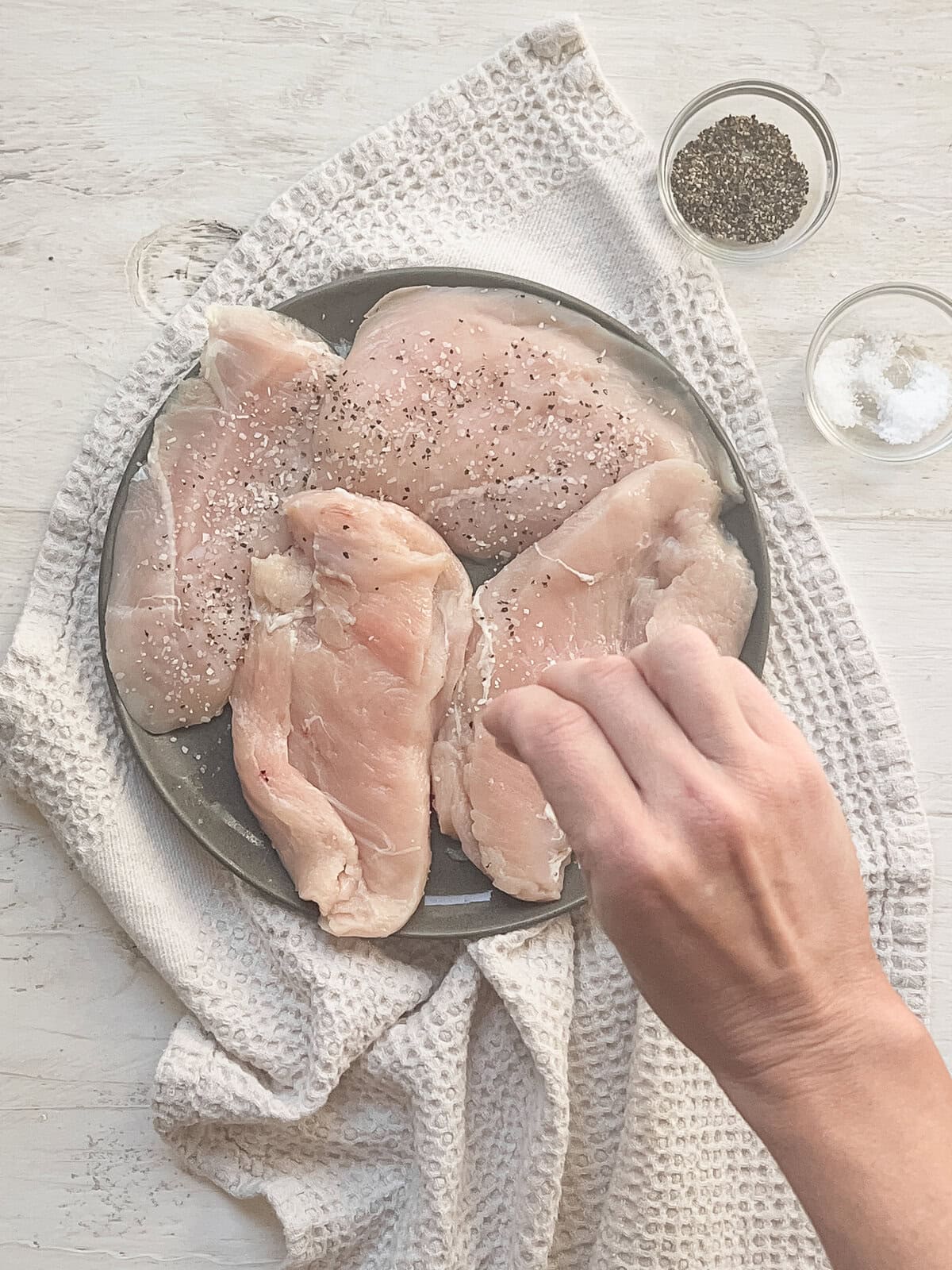 Salt and pepper being sprinkled on chicken cutlets.