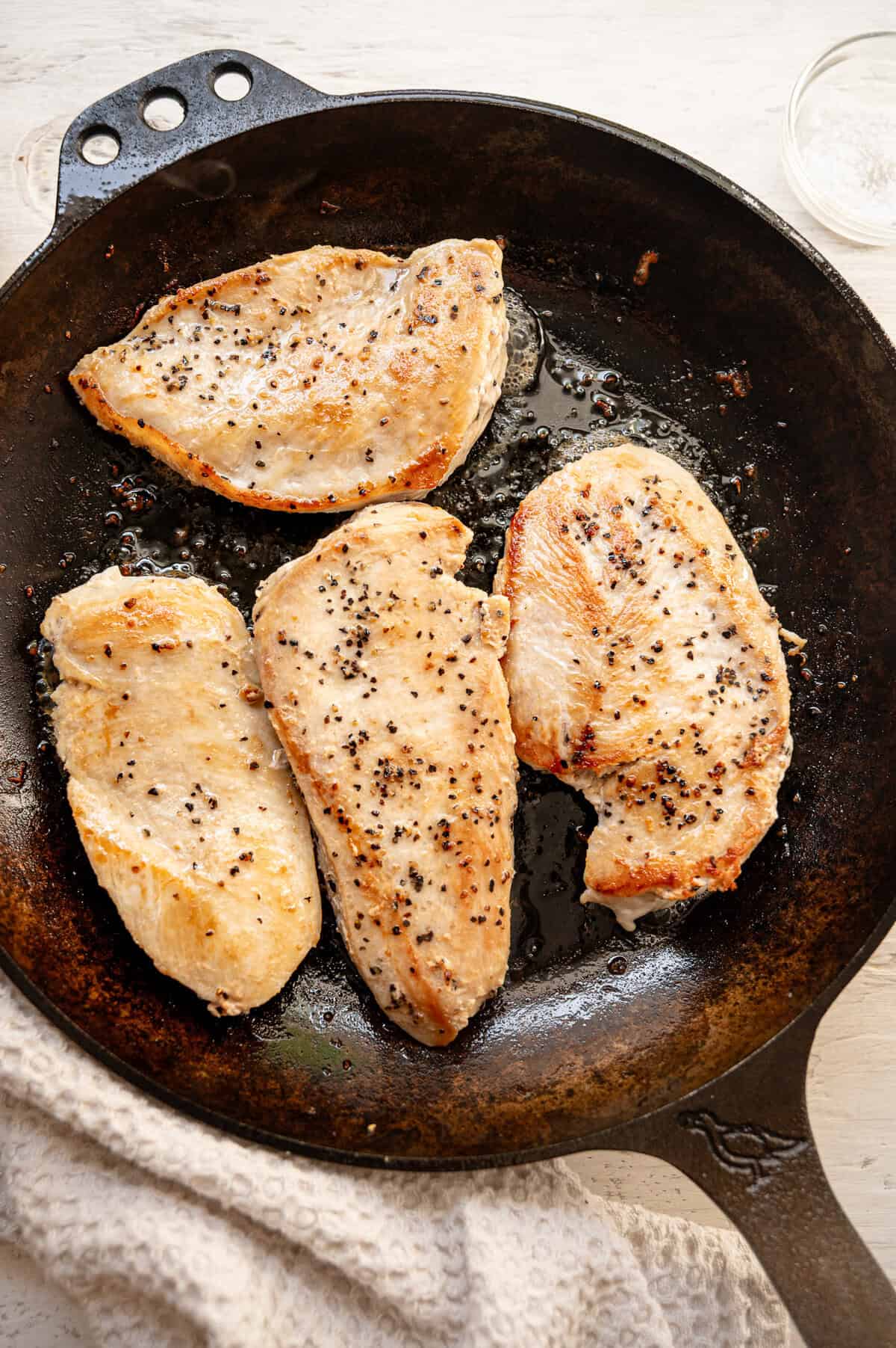 Chicken breast cutlets being sauteed in a cast iron skillet.