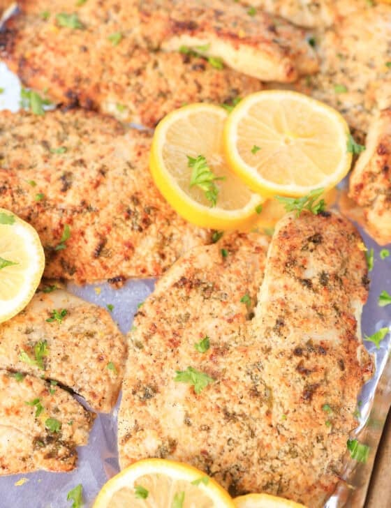 Broiled Parmesan tilapia served with lemon slices and fresh parsley sprinkled on top.