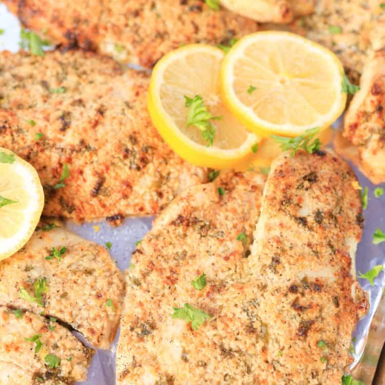 Broiled Parmesan tilapia served with lemon slices and fresh parsley sprinkled on top.