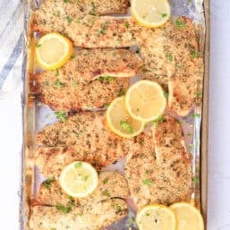 Broiled Parmesan tilapia served on a foil-covered baking sheet with lemon slices and fresh parsley sprinkled on top.