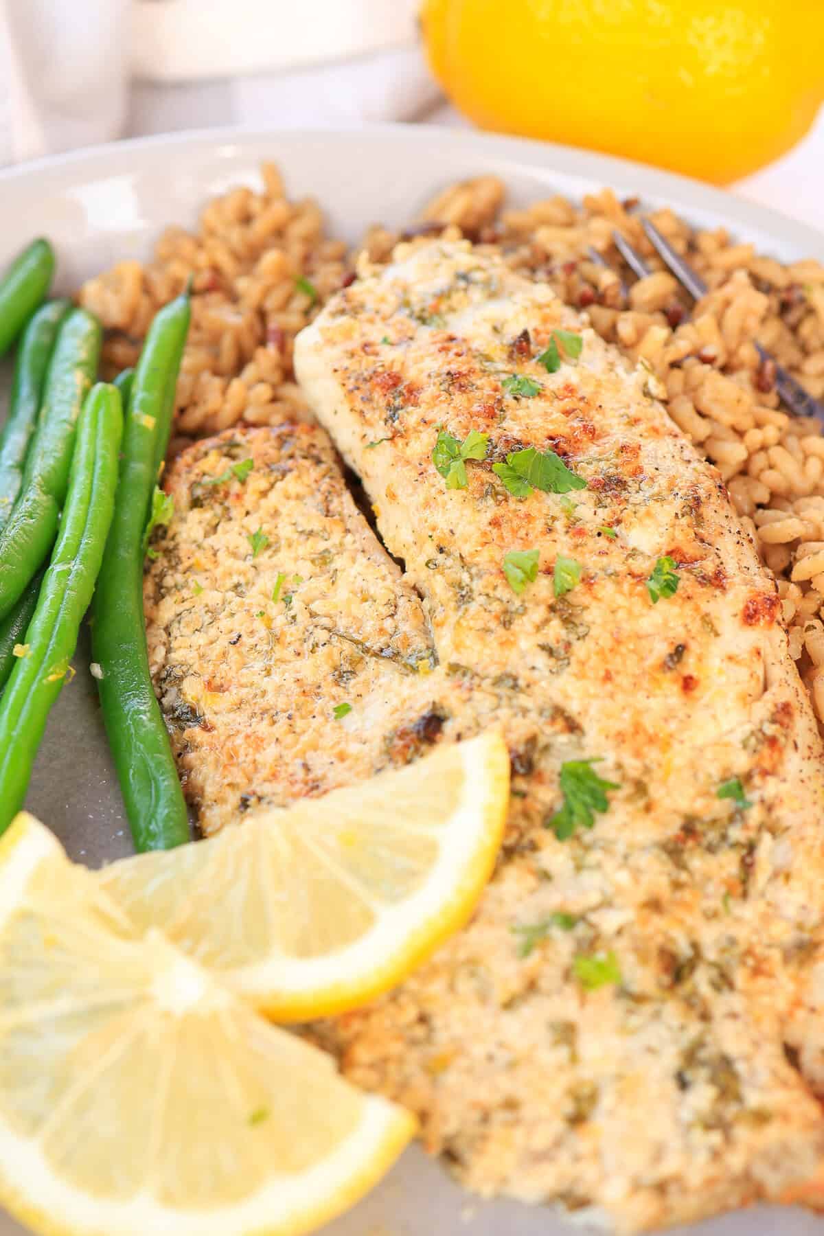 Air fryer tilapia on top of brown rice and steamed green beans on a plate.