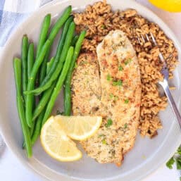 A plate with a broiled Parmesan tilapia filet, steam green beans, and brown rice.