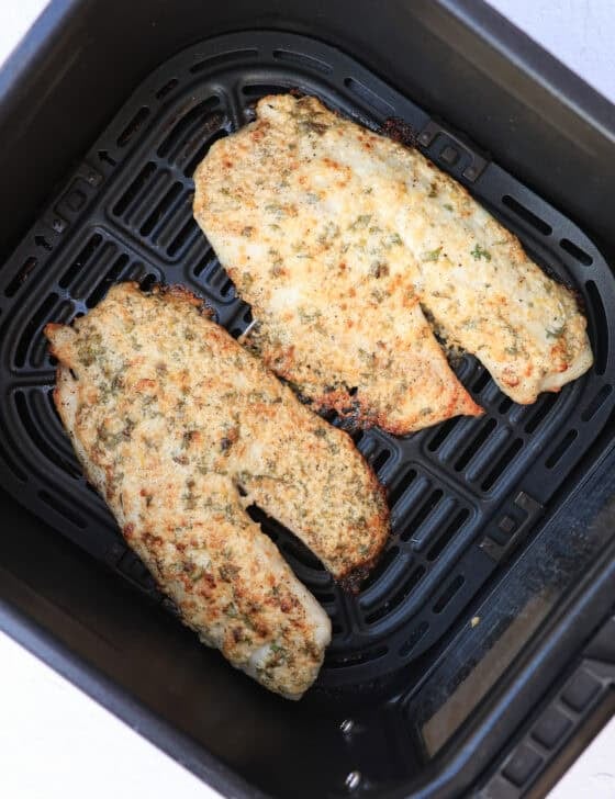 Broiled Parmesan tilapia filets still in an air fryer basket after cooking.