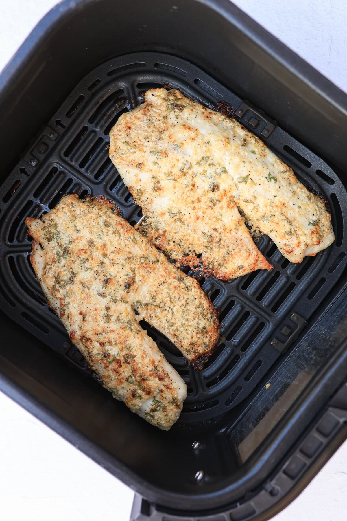 Broiled Parmesan tilapia filets still in an air fryer basket after cooking.