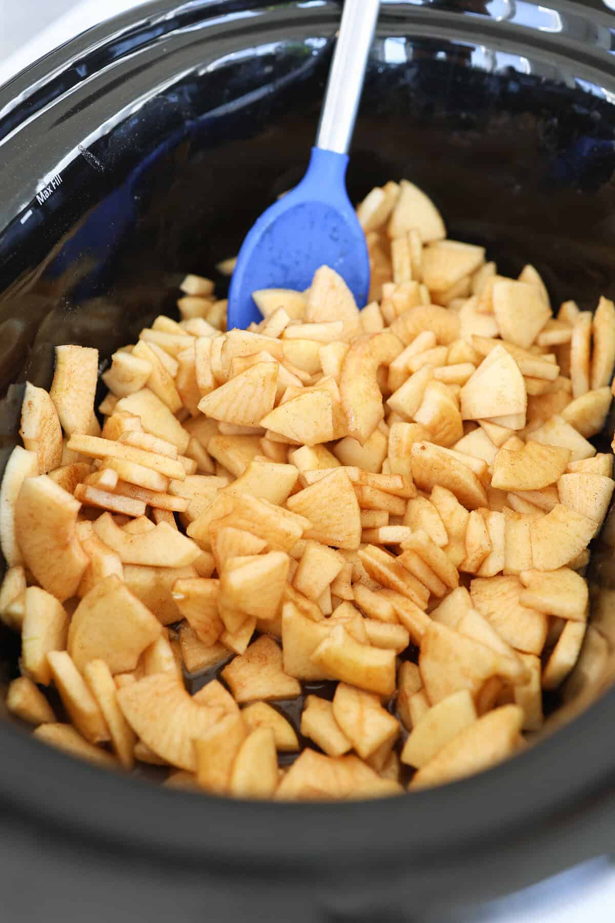 Cinnamon and brown sugar being stirred into a crockpot of chopped apples.