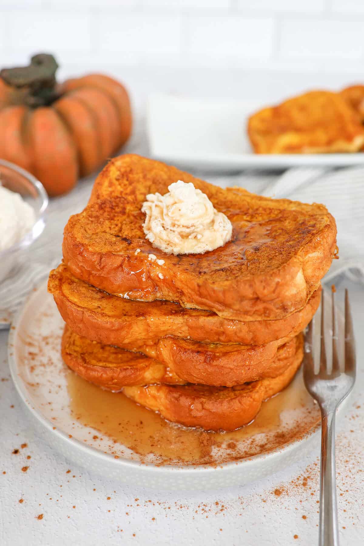 A stack of pumpkin french toast with whipped butter and maple syrup on top.