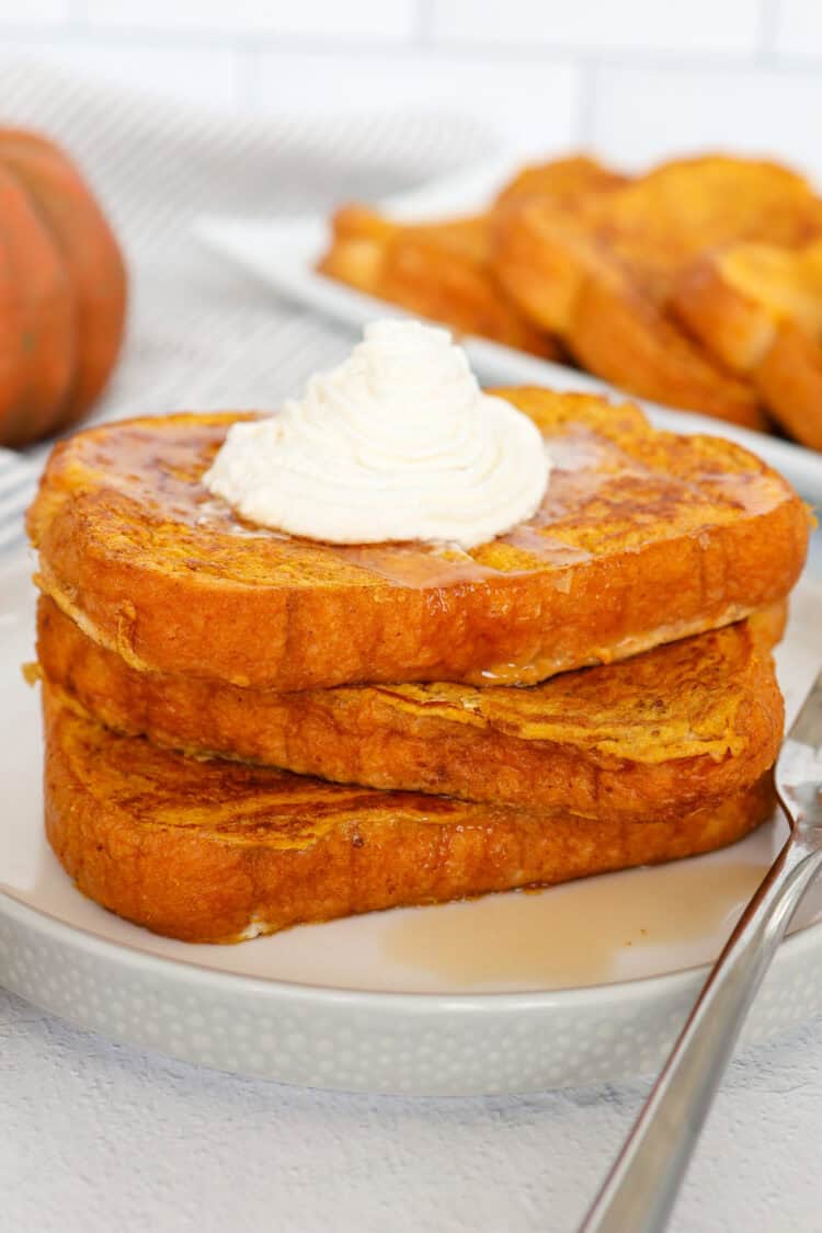 Pumpkin french toast on a plate with maple syrup and whipped cream on top.