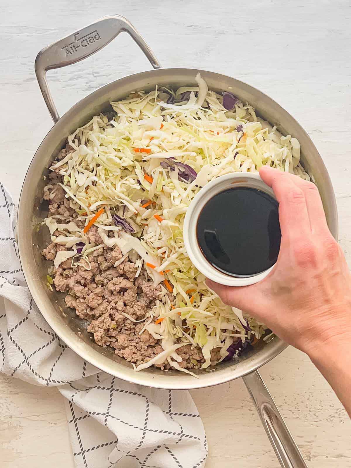 Cooked ground pork, and shredded cabbage in carrots in a skillet with an egg roll sauce about to be poured on top.