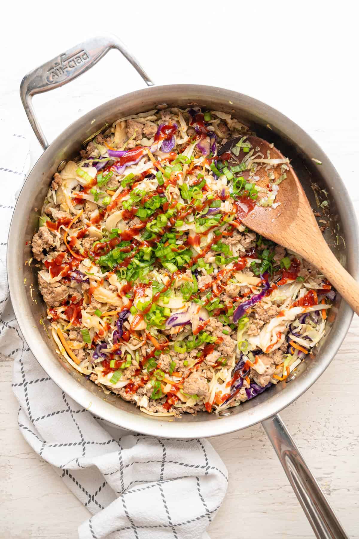Egg roll in a bowl recipe ready to serve from a skillet with siracha drizzled all over it.