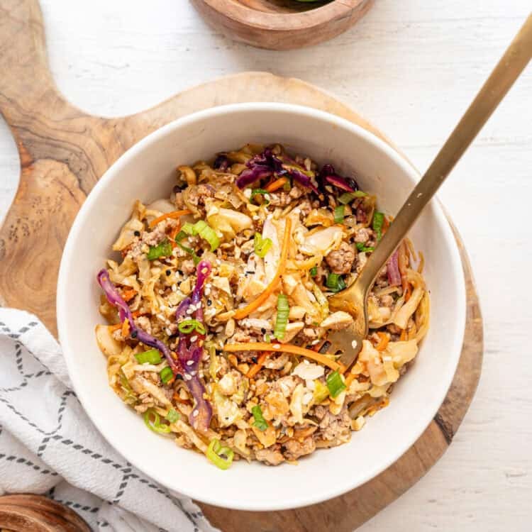 Egg roll in a bowl served in a white bowl on a wooden cutting board.