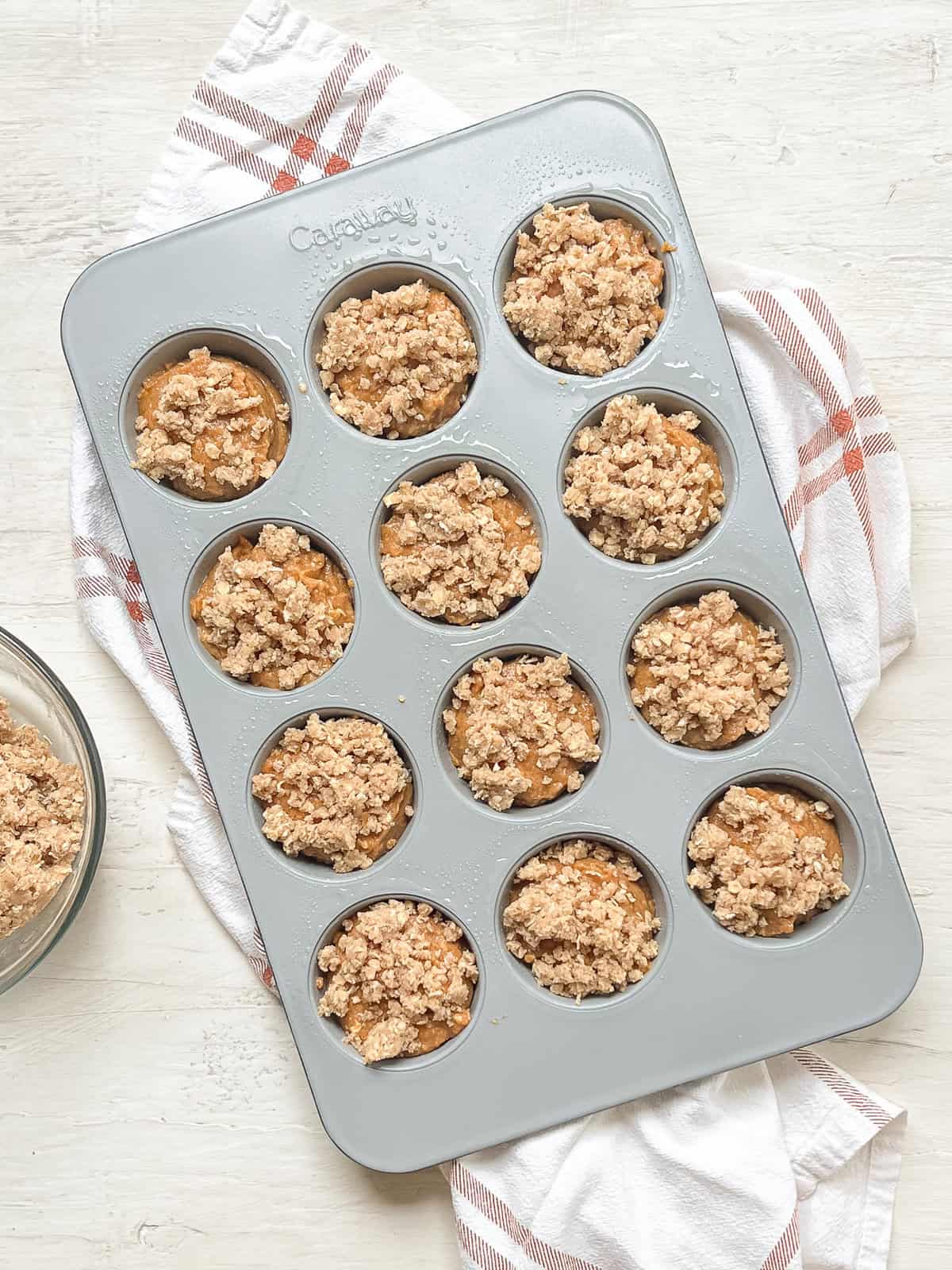 Batter for pumpkin muffins in a muffin tin with a crumble topping before baking.