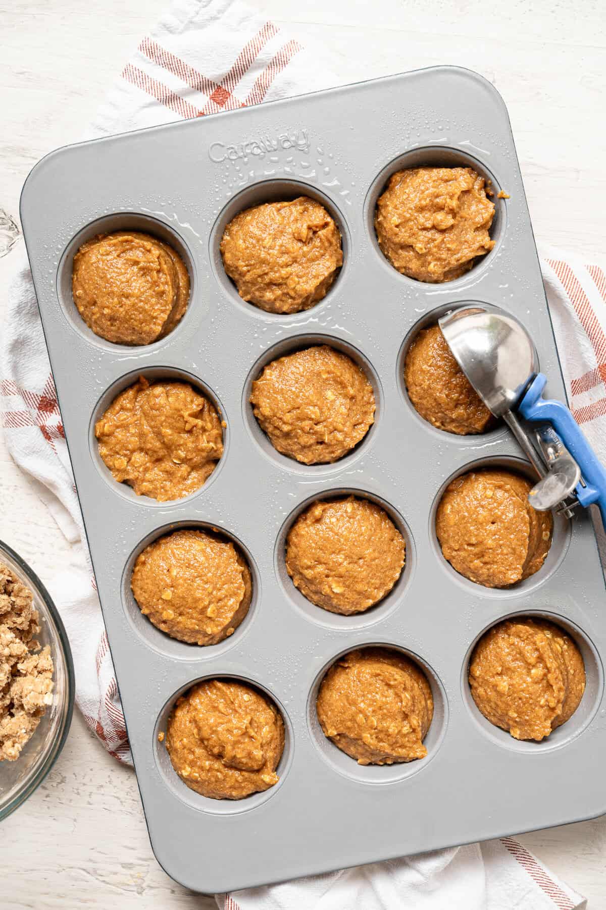 Pumpkin muffin batter being scooped into a muffin tin.