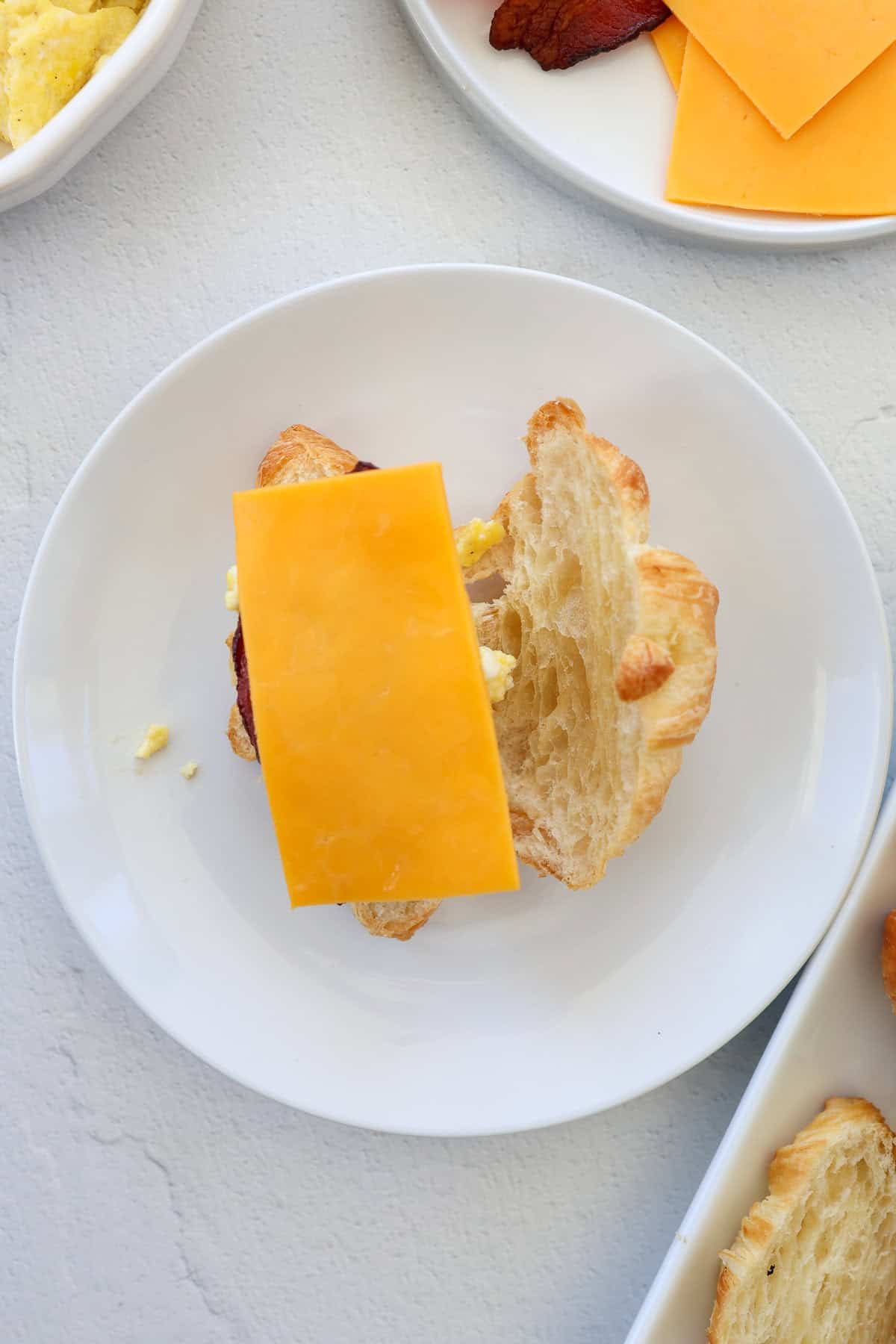 A croissant split in half with eggs, bacon, and a slice of cheese on it.