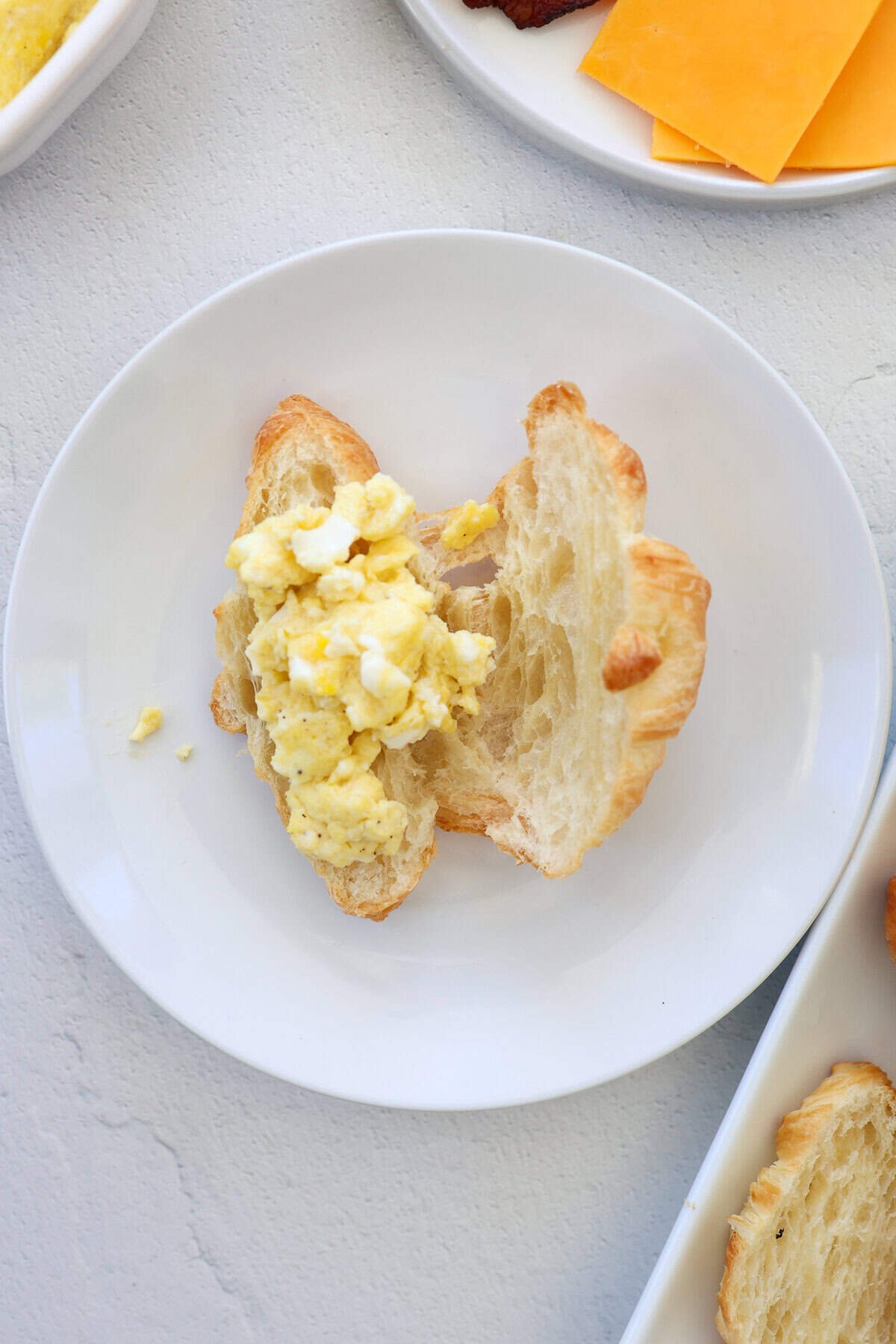 A croissant cut in half with scrambled eggs on it.