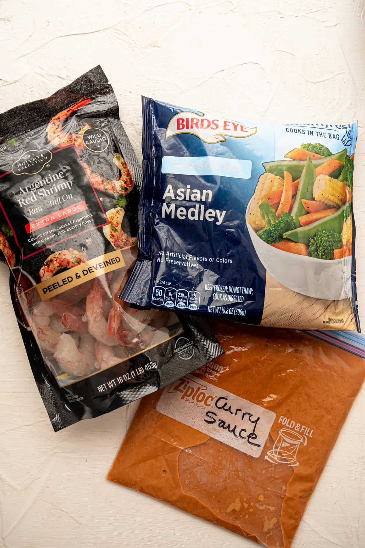 Store-bought bags of frozen shrimp and stir-fry veggies along with a freezer bag labeled curry sauce.