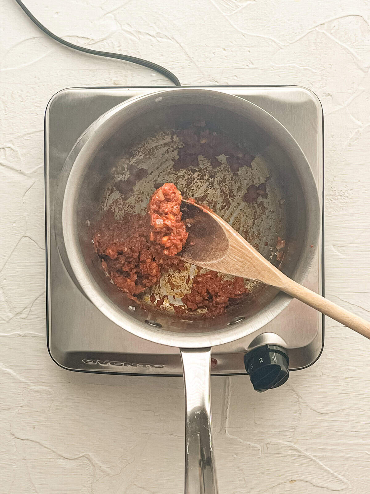 Curry paste being stirred into sauteed onions and ginger in a sauce pan.