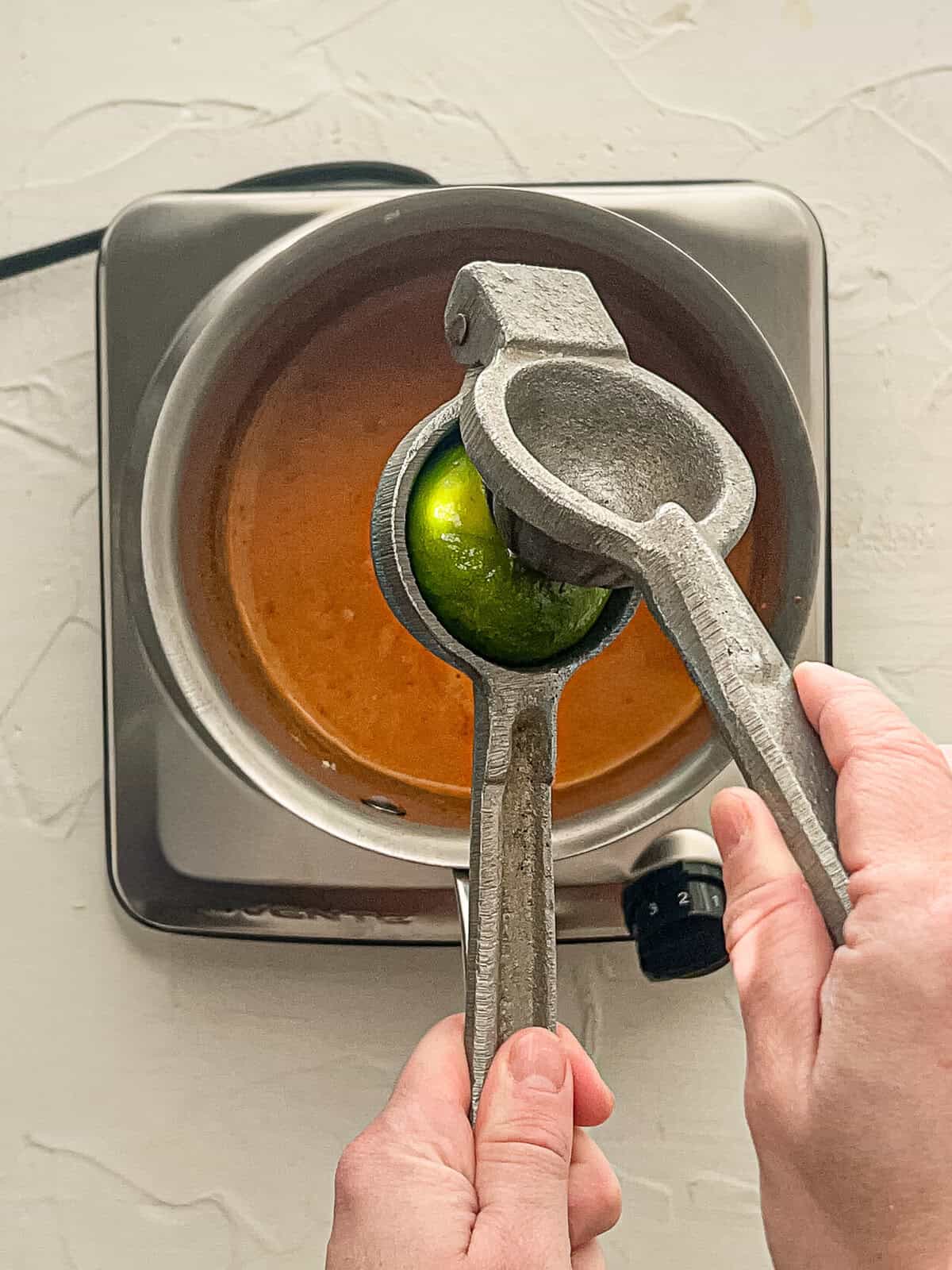 A lime being squeezed into curry sauce in a pan.