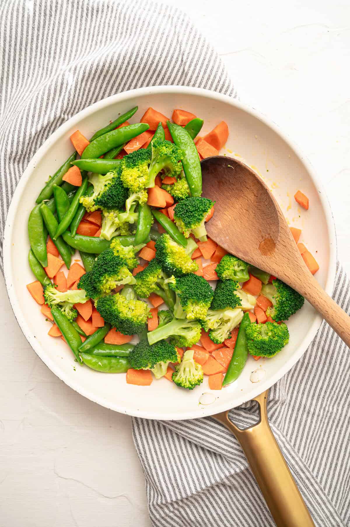 Chopped carrots and broccoli, and snap peas sauteing in a skillet.
