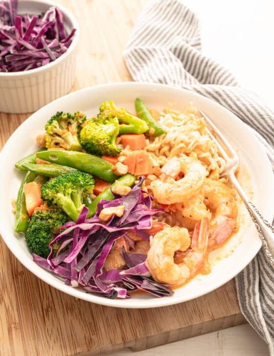 Shrimp curry bowl with stir-fry veggies, cabbage, and chopped peanuts on top.