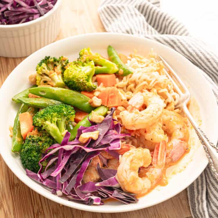 Shrimp curry bowl with stir-fry veggies, cabbage, and chopped peanuts on top.