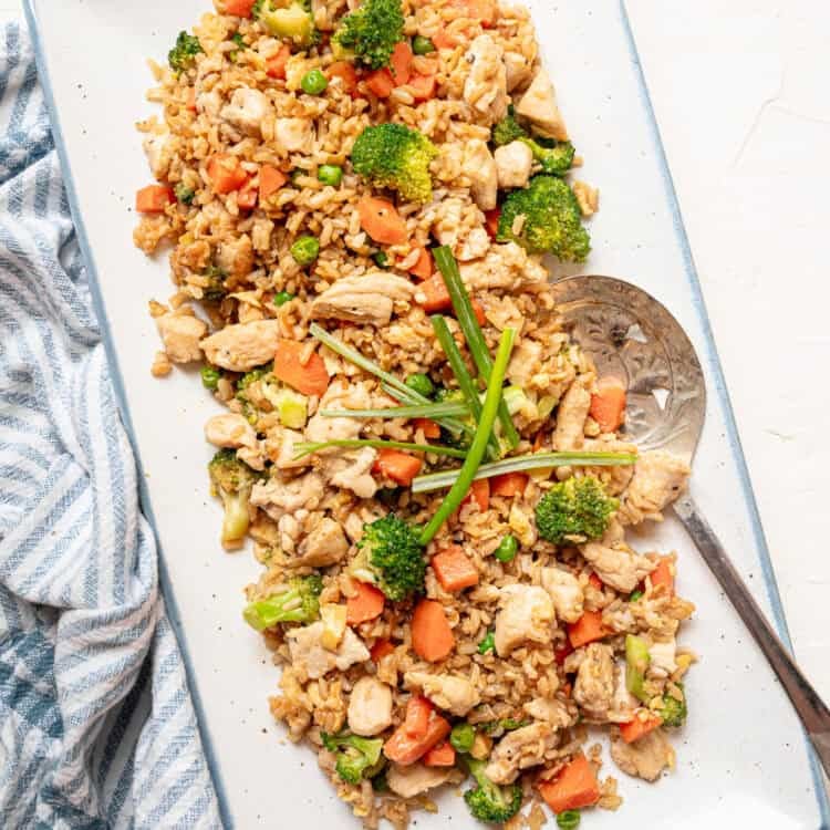 Chicken fried rice served on a rectangle platter with long pieces of green onion on top.