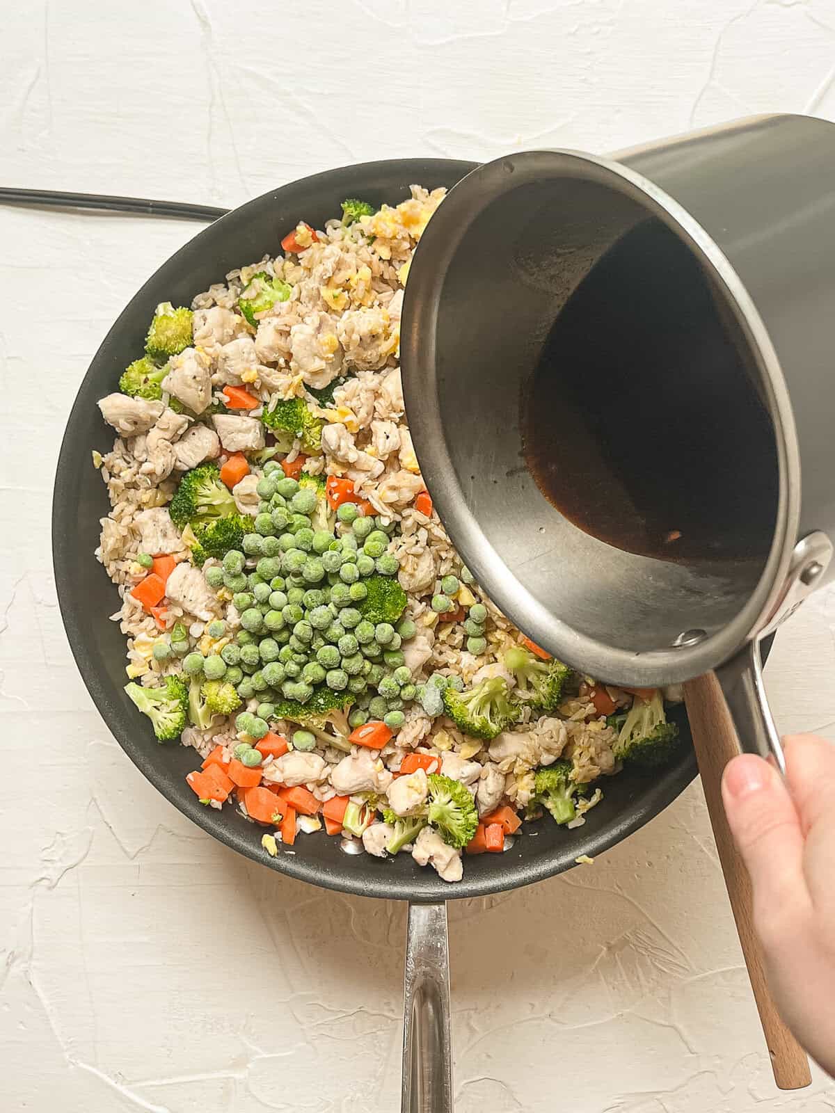 Sweet soy sauce being poured on a skillet of chicken fried rice.