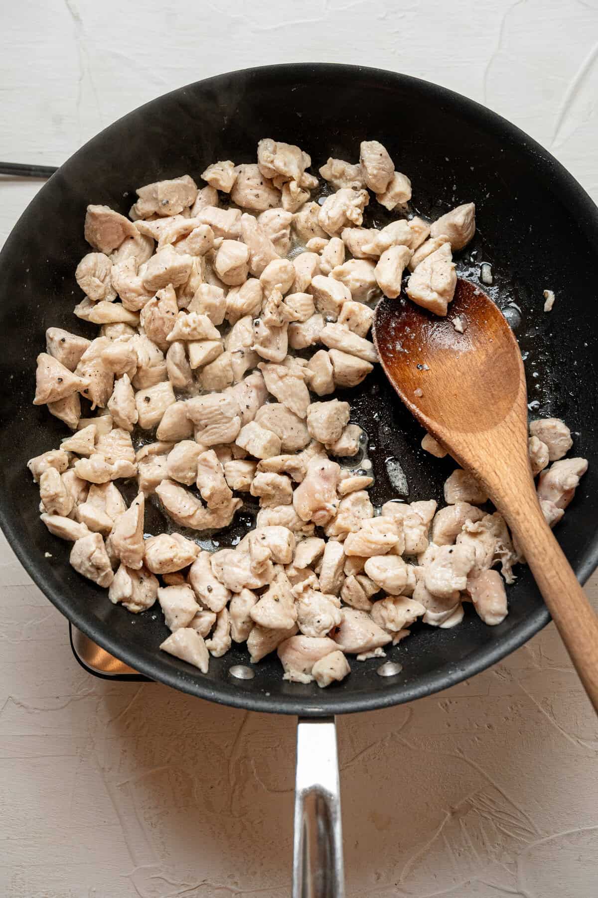 Chopped chicken breasts being sauteed in a skillet.