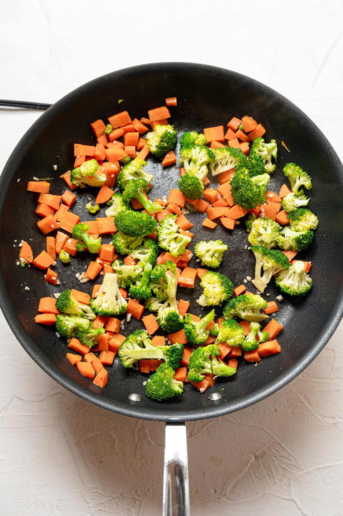 Chopped carrots and broccoli sauteeing in a frying pan.