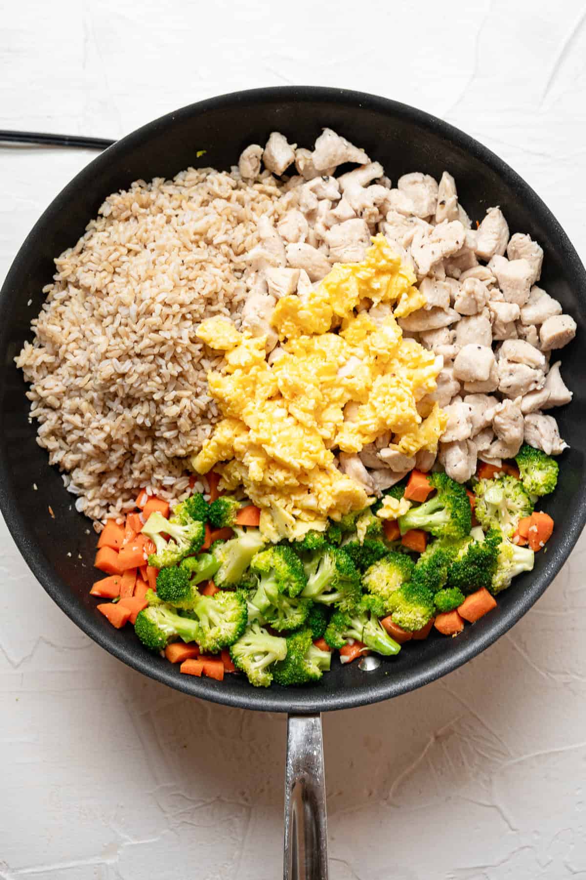 Ingredients for chicken fried rice in separate piles in a skillet.