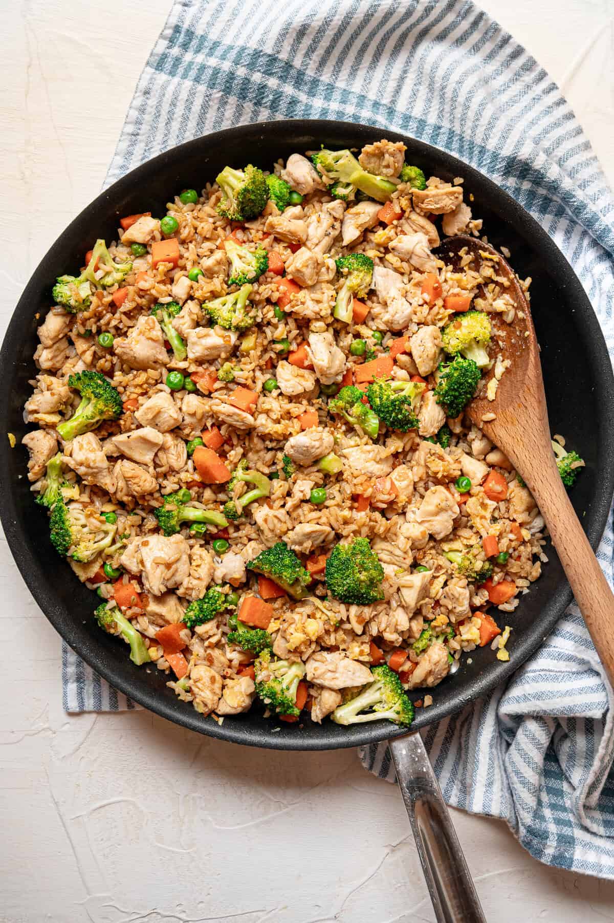 Chicken fried rice served with a wooden spoon out of skillet.