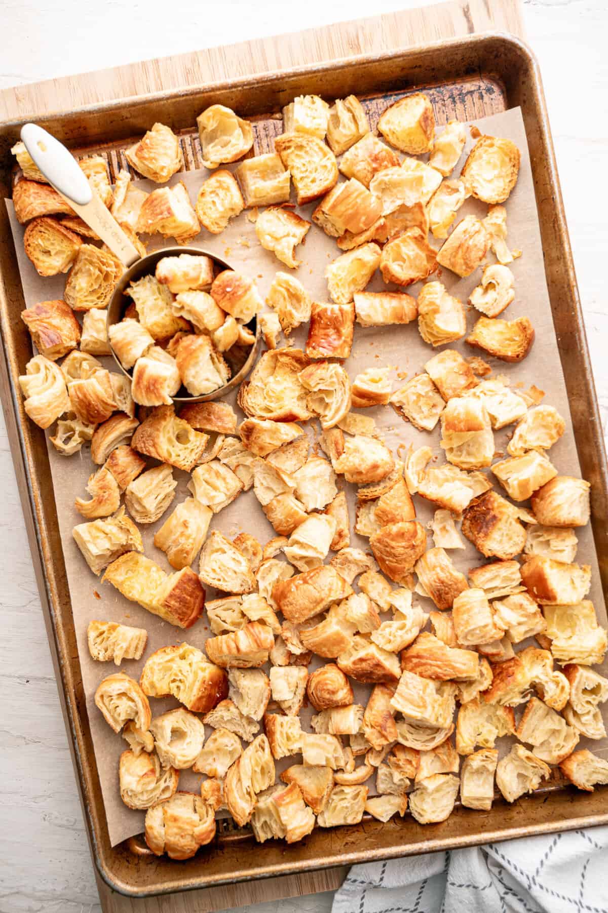 Chopped croissants on a parchment-lined baking sheet.