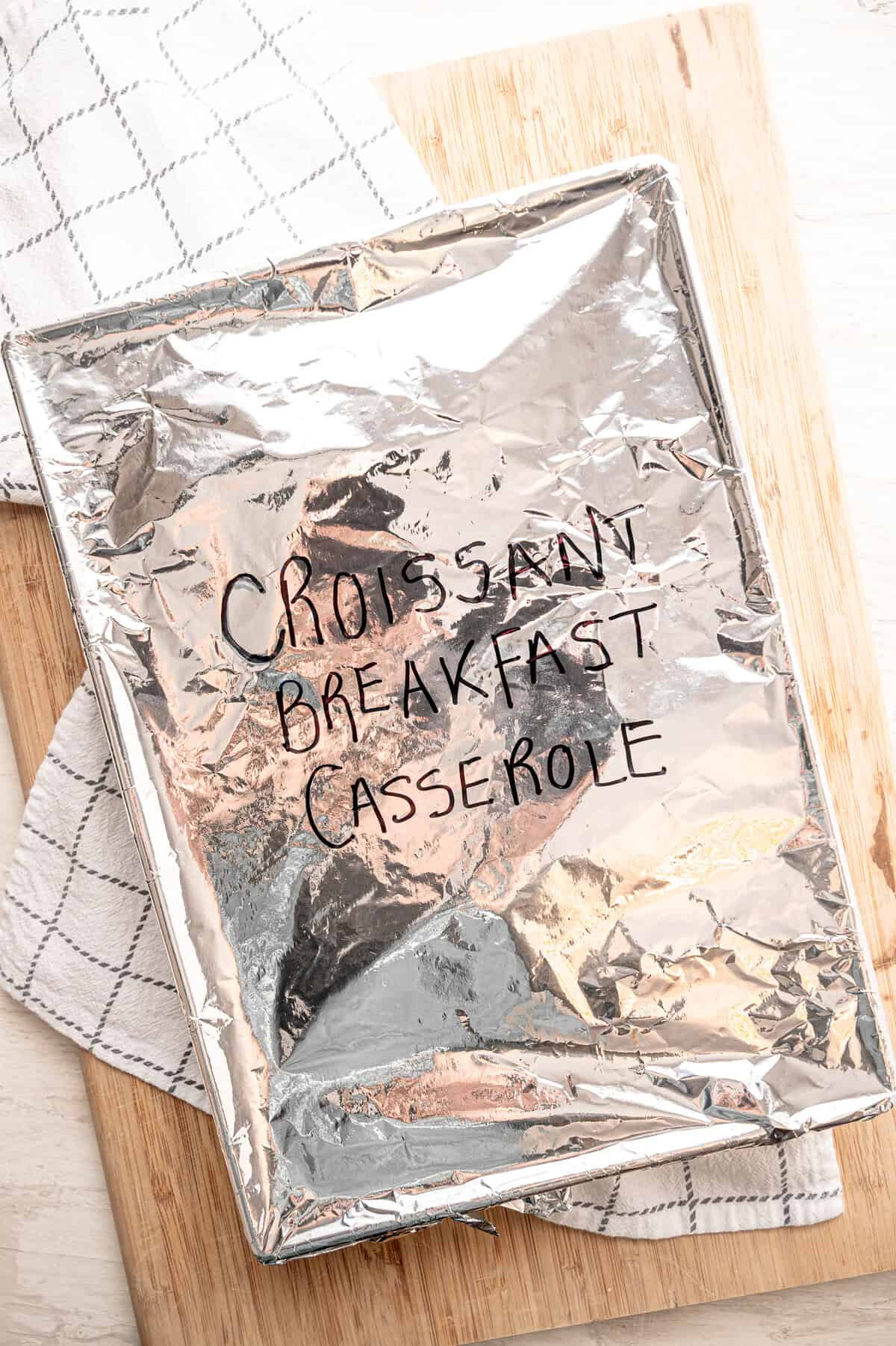 A 9x12-inch baking pan covered in foil and labeled Croissant Breakfast Casserole ready for the freezer.