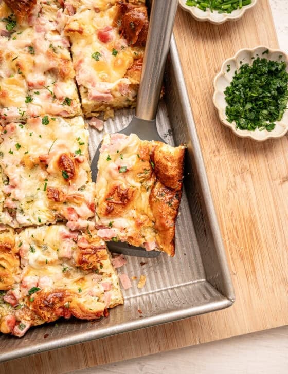 A serving of croissant breakfast casserole being lifted out of a baking dish.