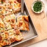 Croissant breakfast casserole being served from a baking dish with fresh herbs on top.