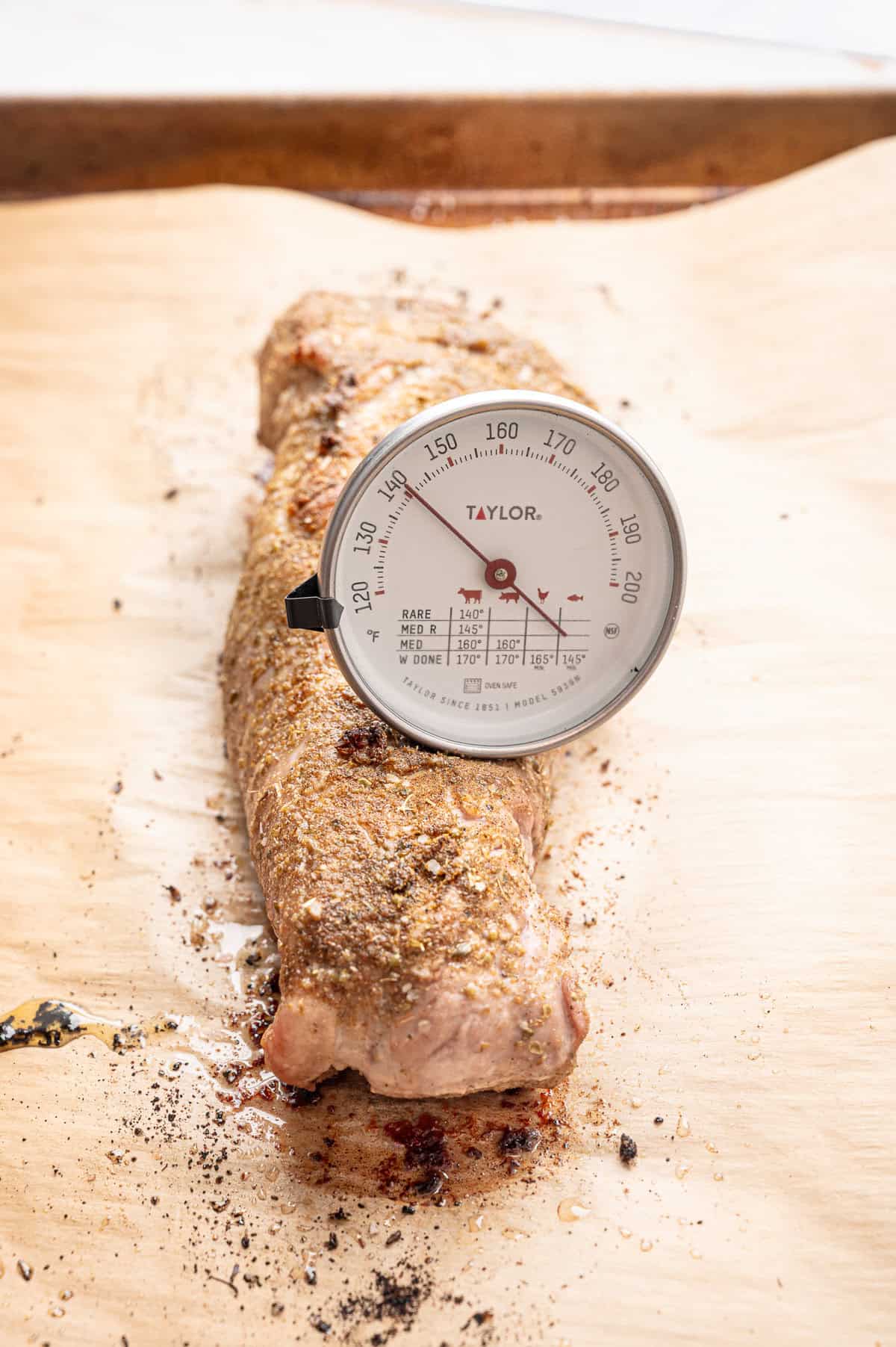 A meat thermometer measuring the temperature of a pork tenderloin on a cutting board.