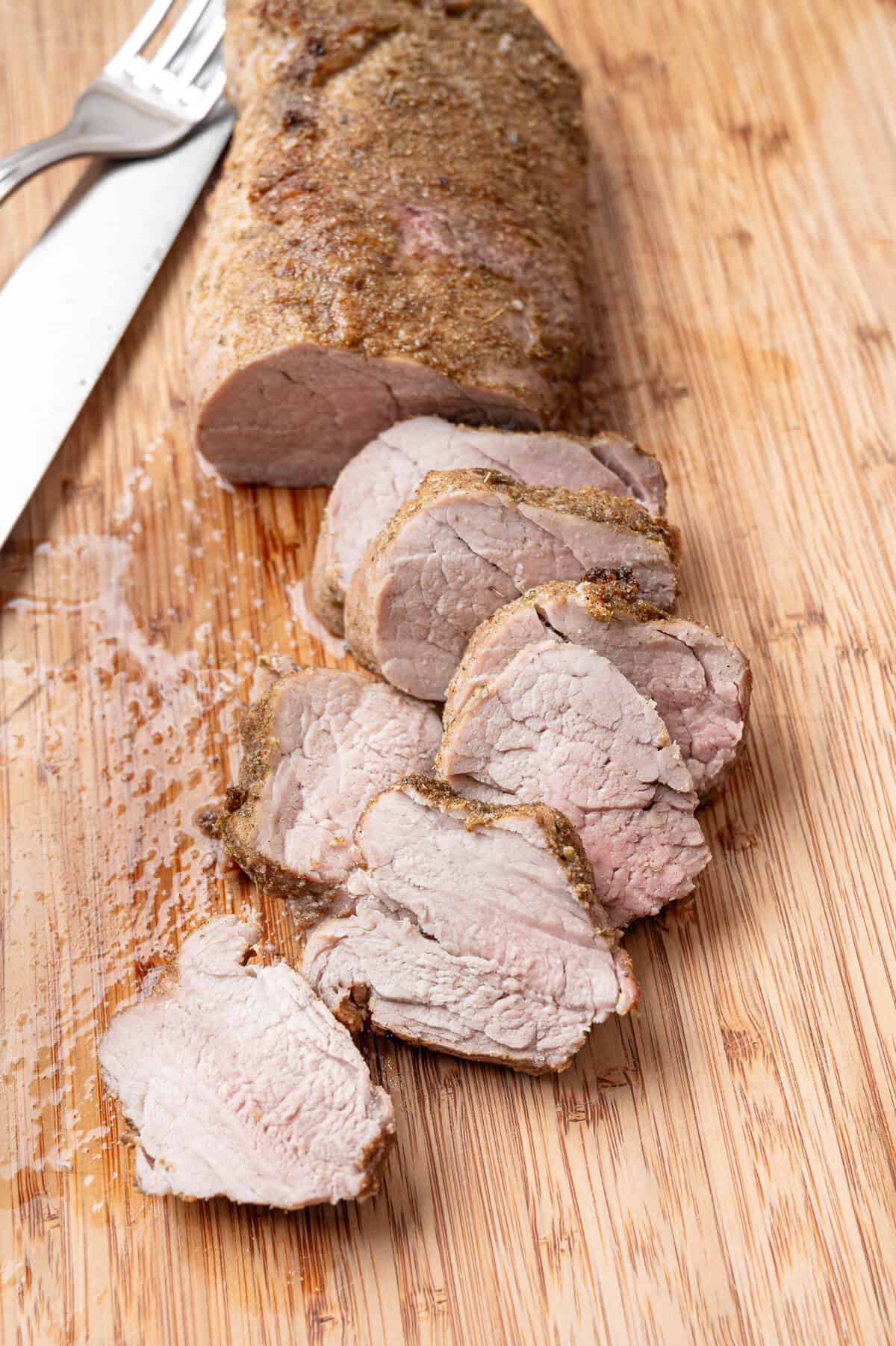 Oven roasted pork tenderloin being sliced on a wooden cutting board.