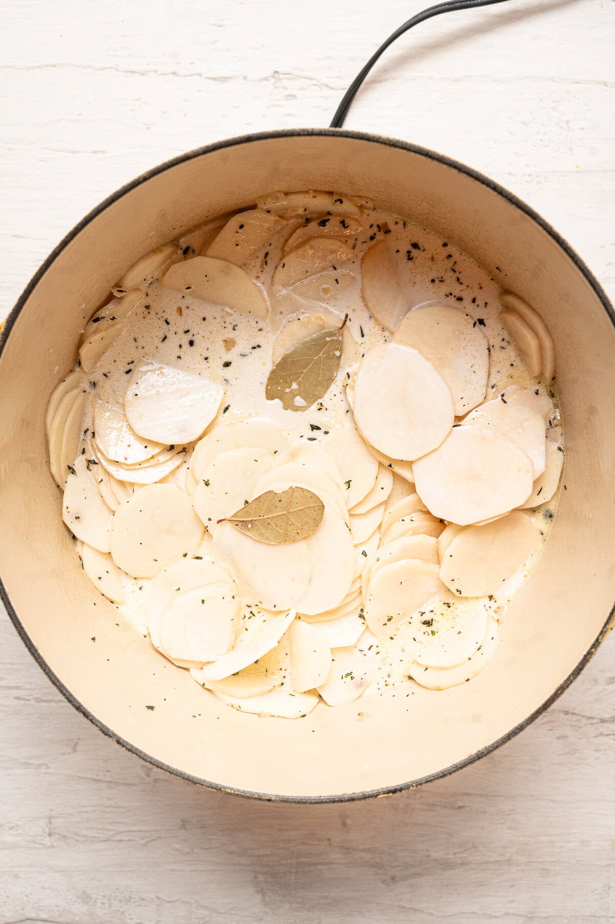 Thinly sliced potatoes in heavy cream with seasonings in a pot.