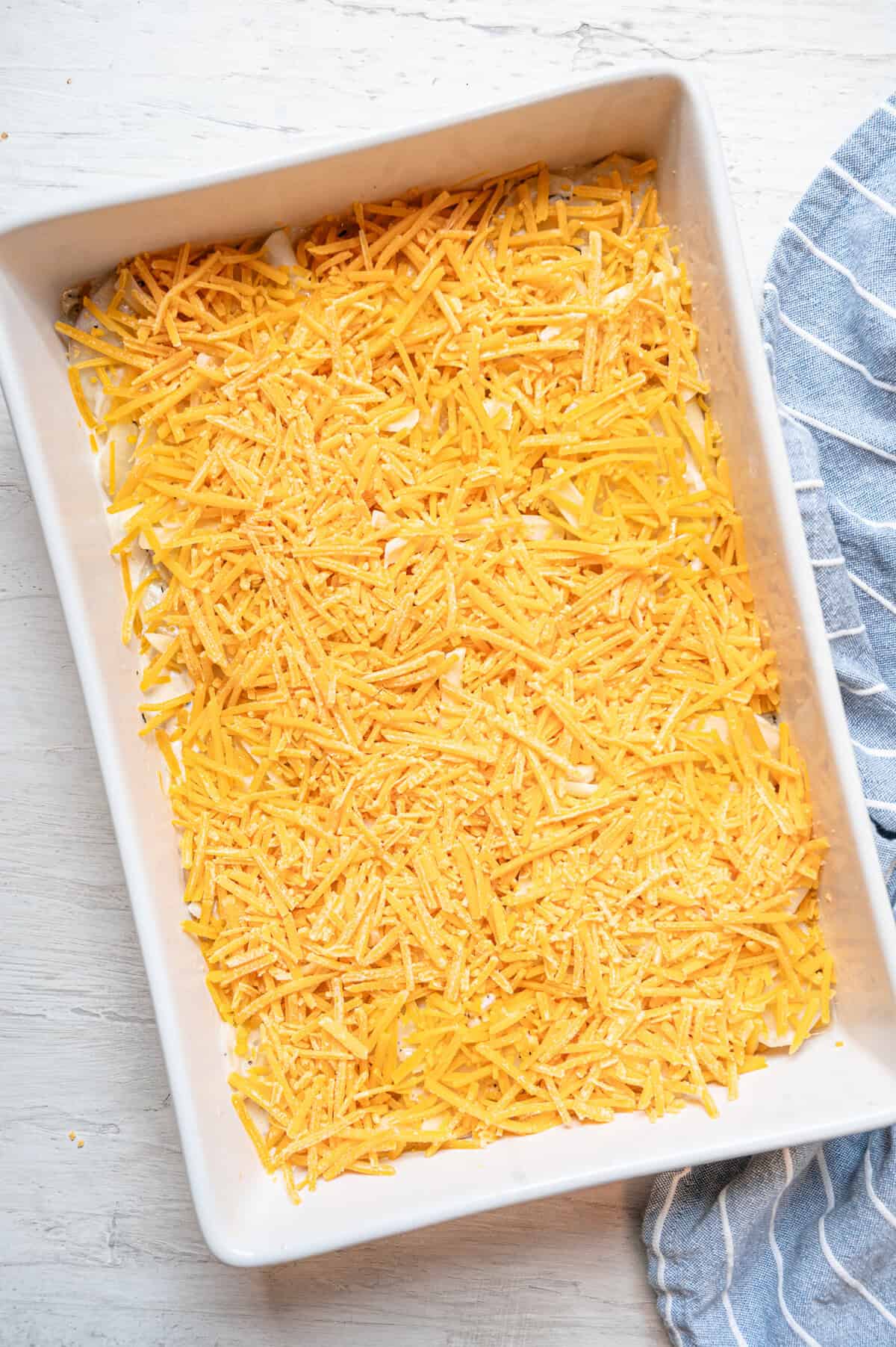 A 9x12 casserole dish layered with thinly sliced potatoes and then shredded cheddar cheese on top.