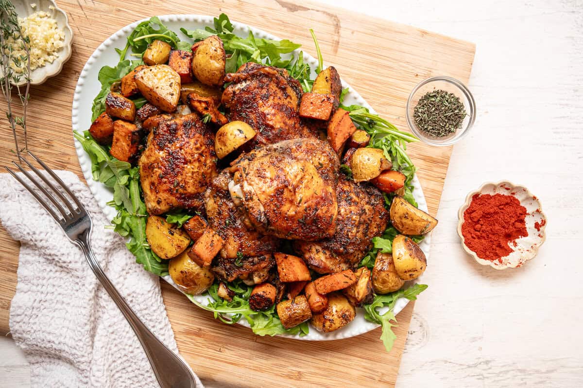 A platter with roasted potatoes and carrots on the outside and bone-in, skin-on chicken thighs piled in the middle.