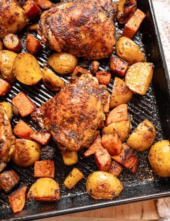 Bone-in, skin-on chicken thighs and chopped potatoes and carrots on a sheet pan out of the oven.