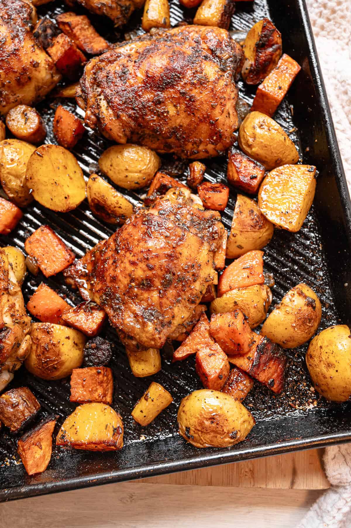 Bone-in, skin-on chicken thighs and chopped potatoes and carrots on a sheet pan out of the oven.